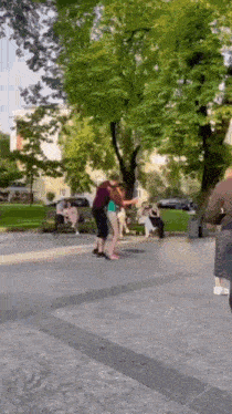a man and woman are dancing in a park with people sitting on benches in the background