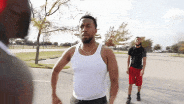 a man in a white tank top talks to another man
