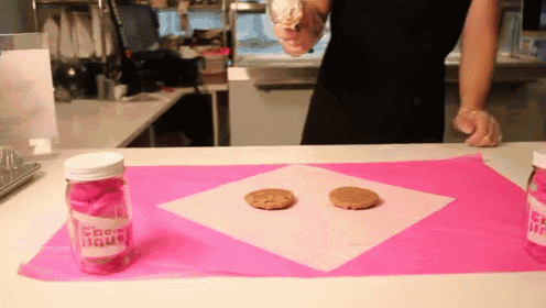 two cookies are sitting on a table next to a jar that says cream puffs