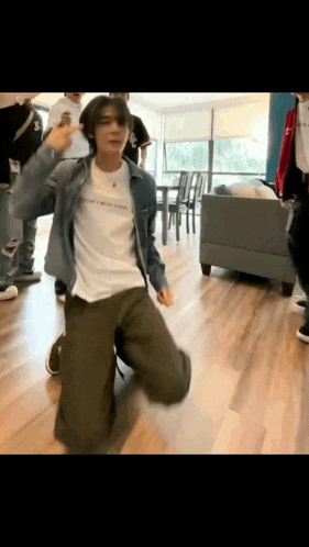 a man in a denim jacket is kneeling down and dancing in a room .