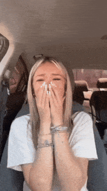 a woman in a white shirt is covering her face with her hands