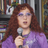 a woman with red hair is holding a microphone and wearing glasses
