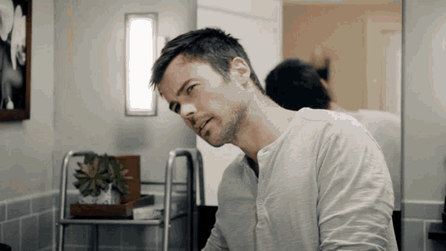 a man in a white shirt looks at himself in the mirror