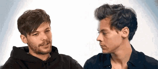 harry styles and louis tomlinson are looking at each other while sitting next to each other .