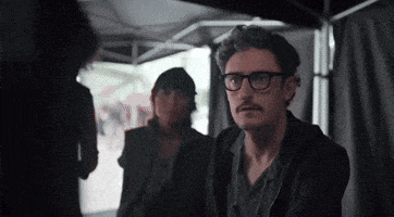 a man wearing glasses and a mustache is sitting in a dark room .