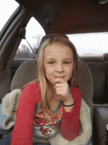 a young girl wearing a kansas city chiefs shirt sits in a car