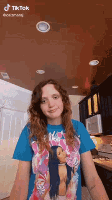 a woman in a blue t-shirt with a picture of nicki minaj on it is standing in a kitchen .