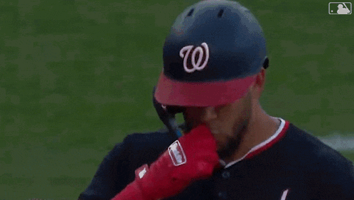 a baseball player is wearing red gloves and a helmet while taking a picture of himself .