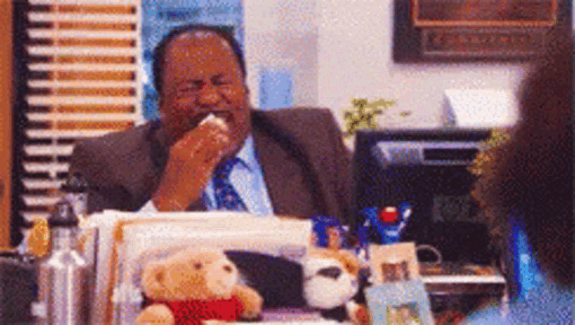 a man in a suit is sitting at a desk with stuffed animals on it