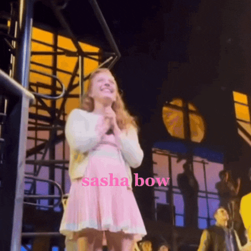 a girl in a pink dress stands on a stage with the name sasha bow above her