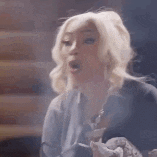 a woman with blonde hair is smoking a cigarette in a dark room .