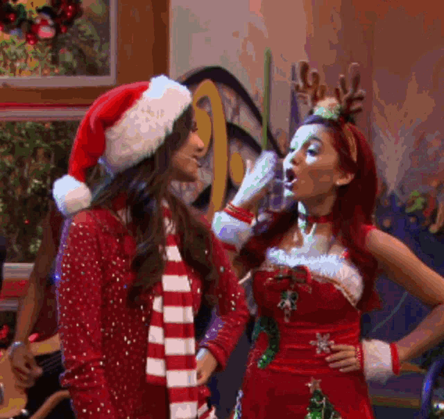 a woman wearing a santa hat is talking to another woman in a christmas outfit