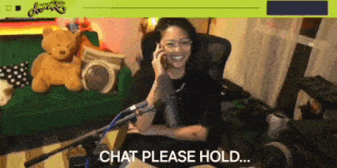 a woman is sitting in front of a microphone talking on a cell phone and says chat please hold ..