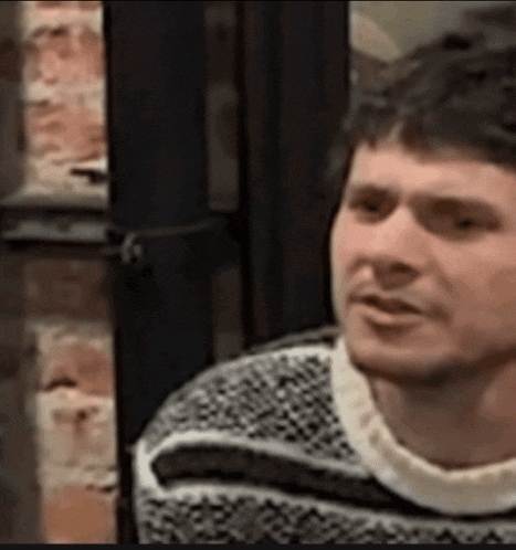 a man in a sweater is sitting in front of a window