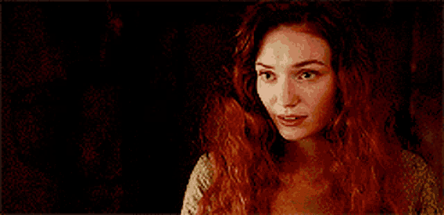 a woman with red hair and blue eyes is smiling in a dark room