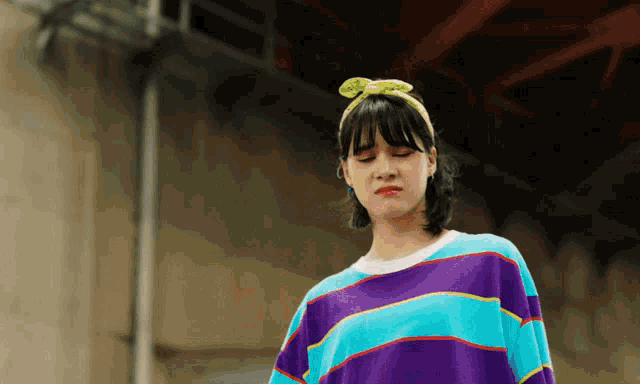 a woman wearing a purple and blue striped shirt and a yellow headband is making a funny face