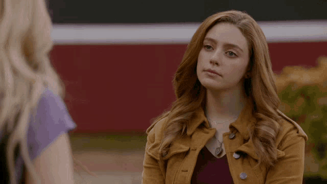 a woman in a brown jacket is standing next to another woman in a purple shirt .
