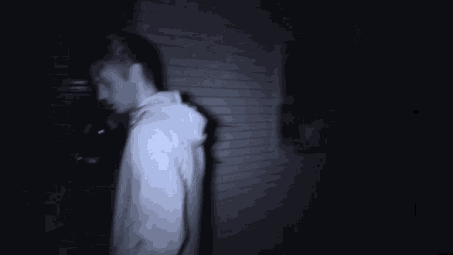 a blurry picture of a man in a white shirt standing in a dark room .