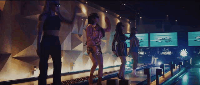a group of women are standing on a bowling alley in a dark room