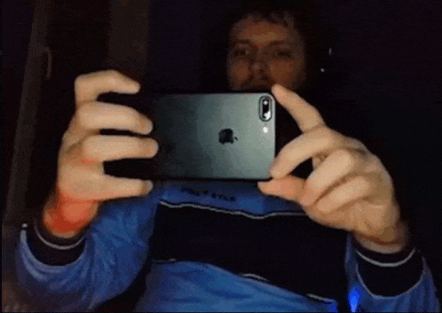 a man in a blue shirt is taking a picture of himself with his iphone