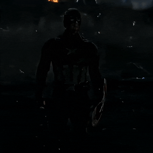 a man in a captain america costume holds a shield in the dark