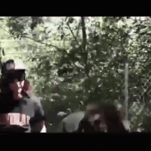 a man is smoking a cigarette in the woods while another man looks on .