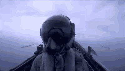 a fighter jet pilot is flying over the ocean in a helmet and goggles .