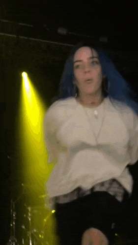 a woman with blue hair is dancing on stage in front of a yellow light