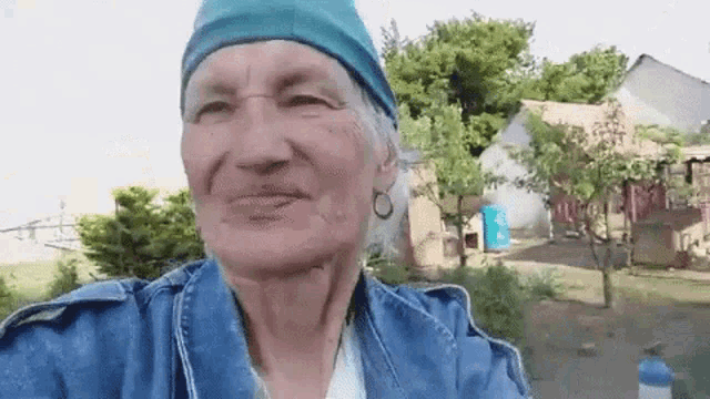 an elderly woman wearing a blue headband and a denim jacket is smiling .