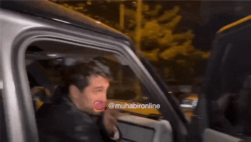 a man is sitting in a car waving his hand and has a watermark that says muhabironline