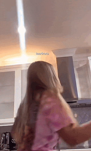 a woman in a pink shirt is standing in a kitchen with a light coming from the ceiling and the words tea4ruts visible