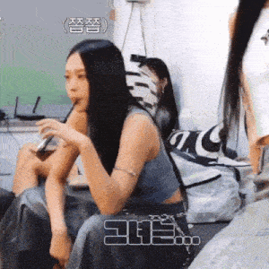a woman with long black hair is sitting on the floor drinking from a straw ..