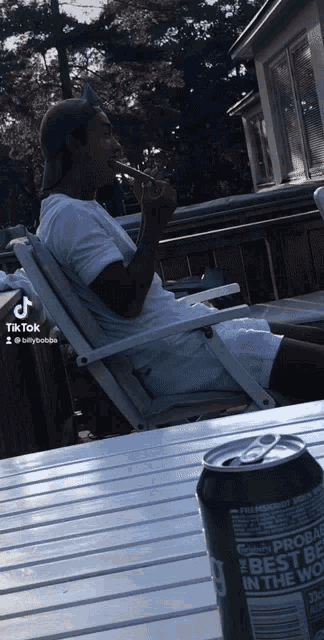 a man sitting in a chair next to a can of soda that says best in the world