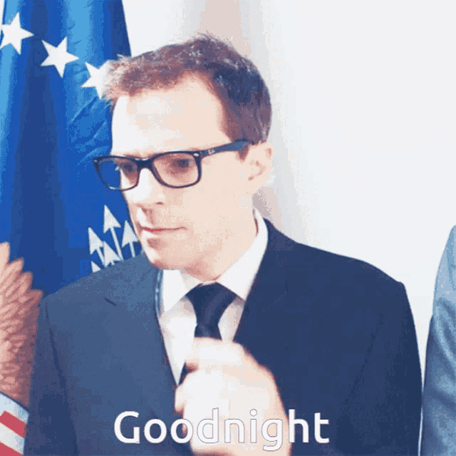 a man in a suit and tie says goodnight in front of a flag