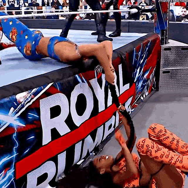 two women are wrestling in front of a royal rumble sign
