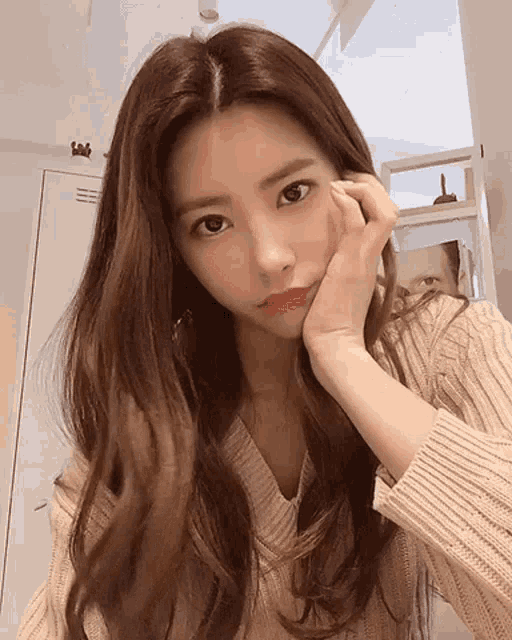 a woman in a sweater holds her hand to her face and looks at the camera
