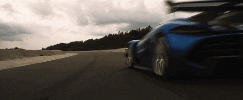 a blue sports car is driving down a road with trees in the background
