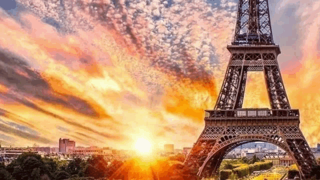 the eiffel tower in paris at sunset with the sun shining through the clouds behind it .