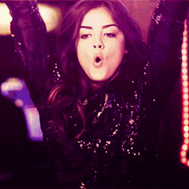 a woman in a black sequined top holds her arms up in the air