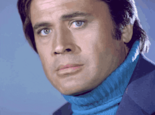 a man wearing a blue turtleneck and a blue jacket looks at the camera