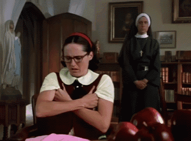 a woman with glasses and a red headband is sitting at a table with her hands on her chest