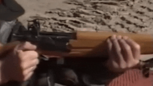 a person is holding a gun in their hands while sitting on the beach .