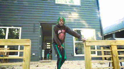 a man with green hair is standing on a wooden fence in front of a large house .