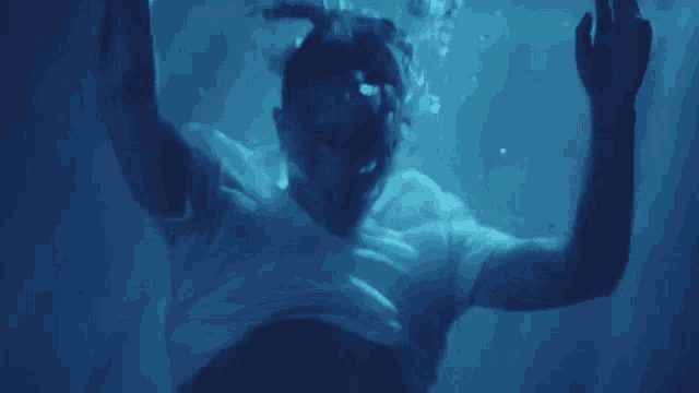 a man in a white shirt is swimming underwater with his hands in the air .