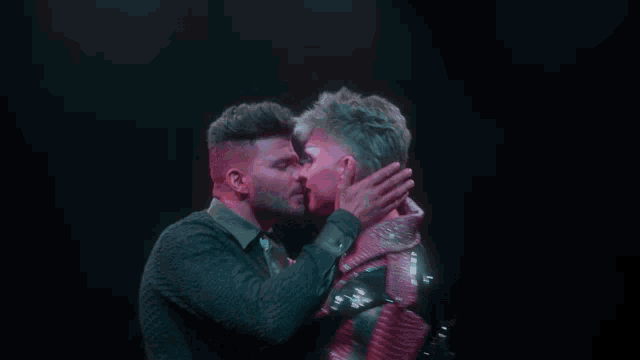 a man with purple paint on his face kisses another man in a red jacket