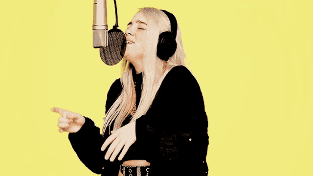 a blonde woman wearing headphones is singing into a microphone .