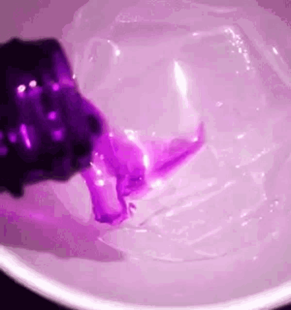a purple object is being poured into a bowl of water .