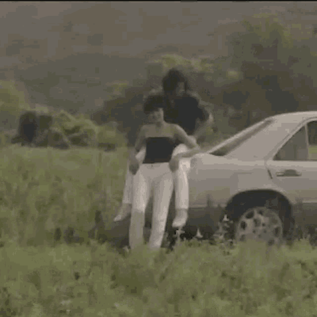 a man and woman are standing next to a car in a grassy field