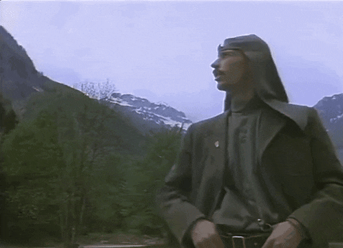 a man in a hooded jacket stands in front of a mountain range