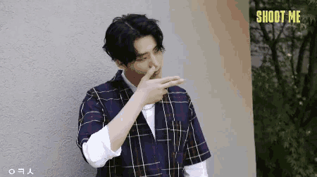 a man wearing a plaid shirt is covering his nose with his hand .